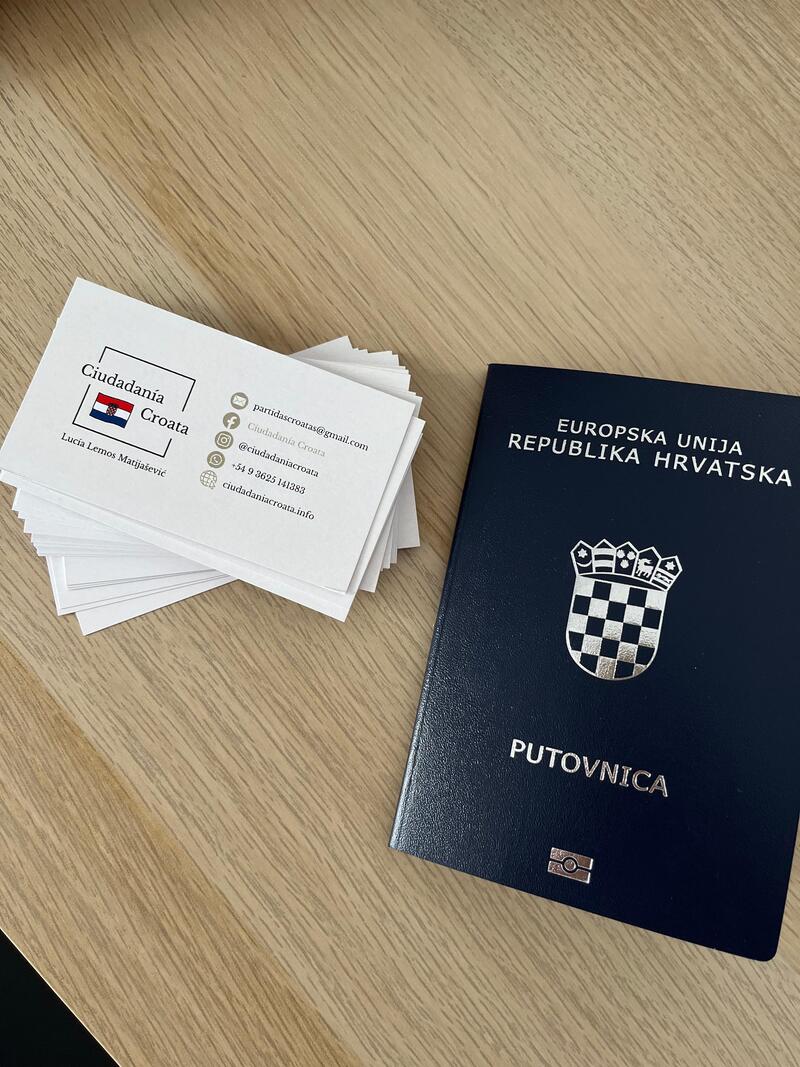 Pasaporte croata junto a tarjetas de contacto de Ciudadanía Croata sobre una mesa de madera